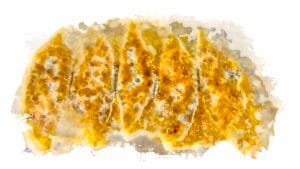 Five pieces of cooked gyoza with a golden crust and lacy wings from the starch in the pan.