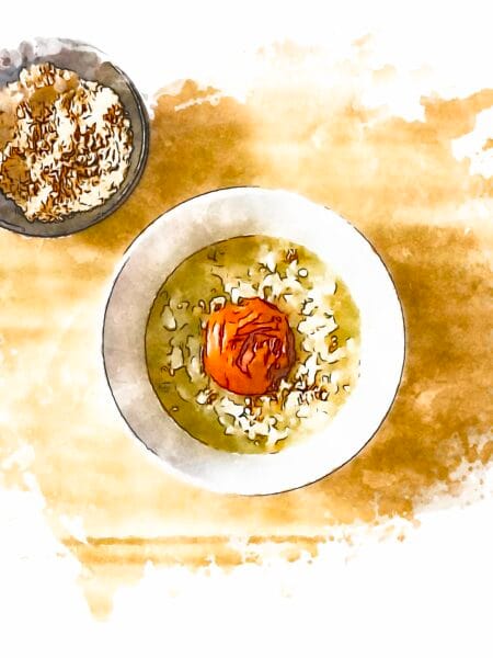 A bowl of okayu rice porridge with an umeboshi plum in the center, and sesame salt served on the side.