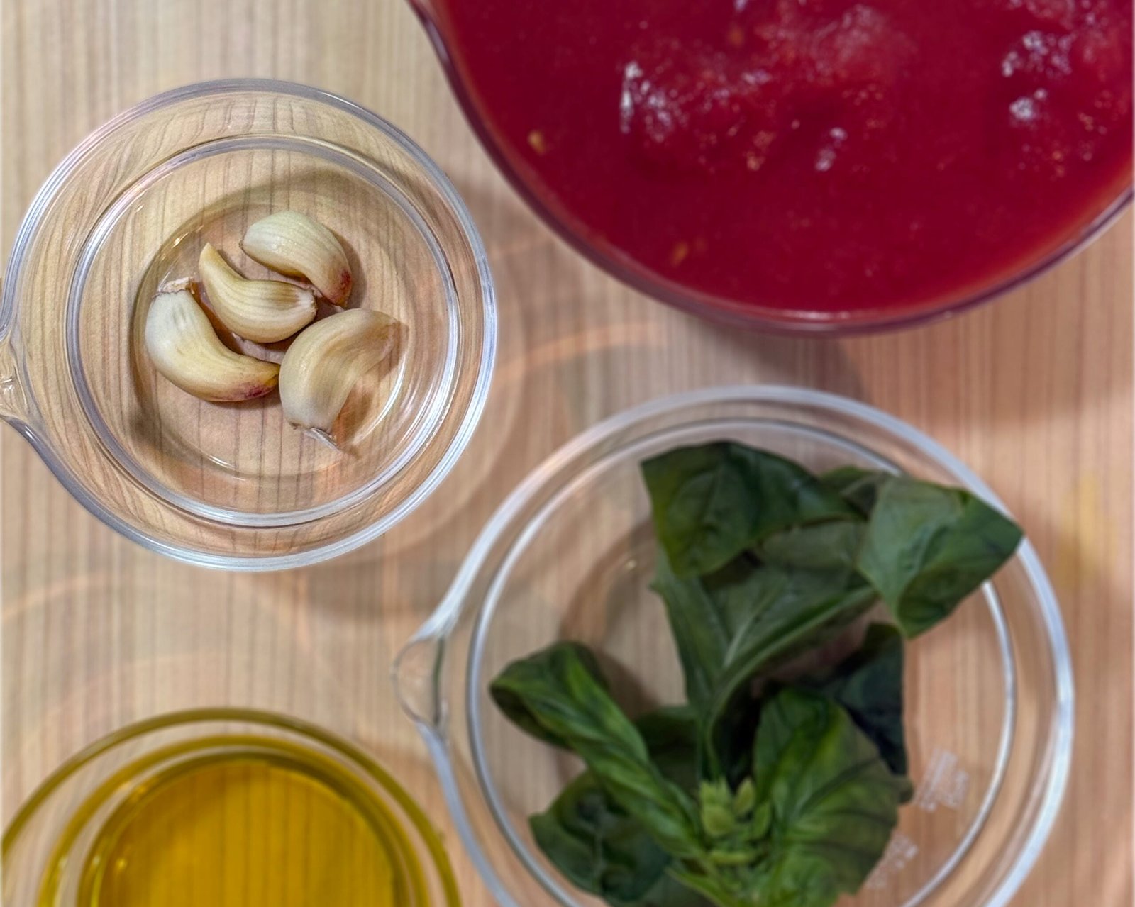 Tomato sauce ingredients — tomato, garlic, basil, and olive oil — arranged on a wooden board.